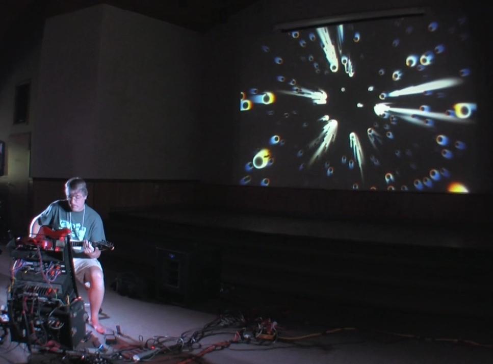 A photo of an electronic music performance with projected visuals of diffracted circle streaks