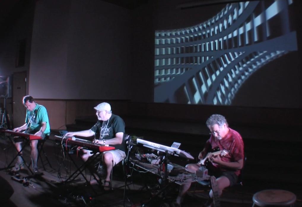 A photo of an electronic music performance with projected visuals of a curved grid
