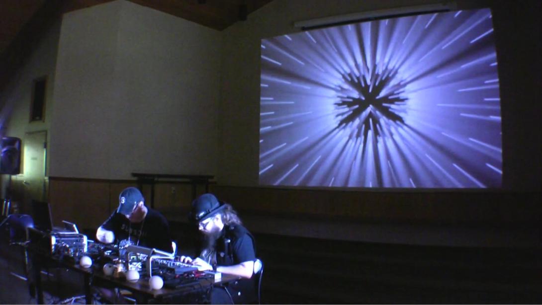 A photo of an electronic music performance with projected visuals of soft blue zooming lines