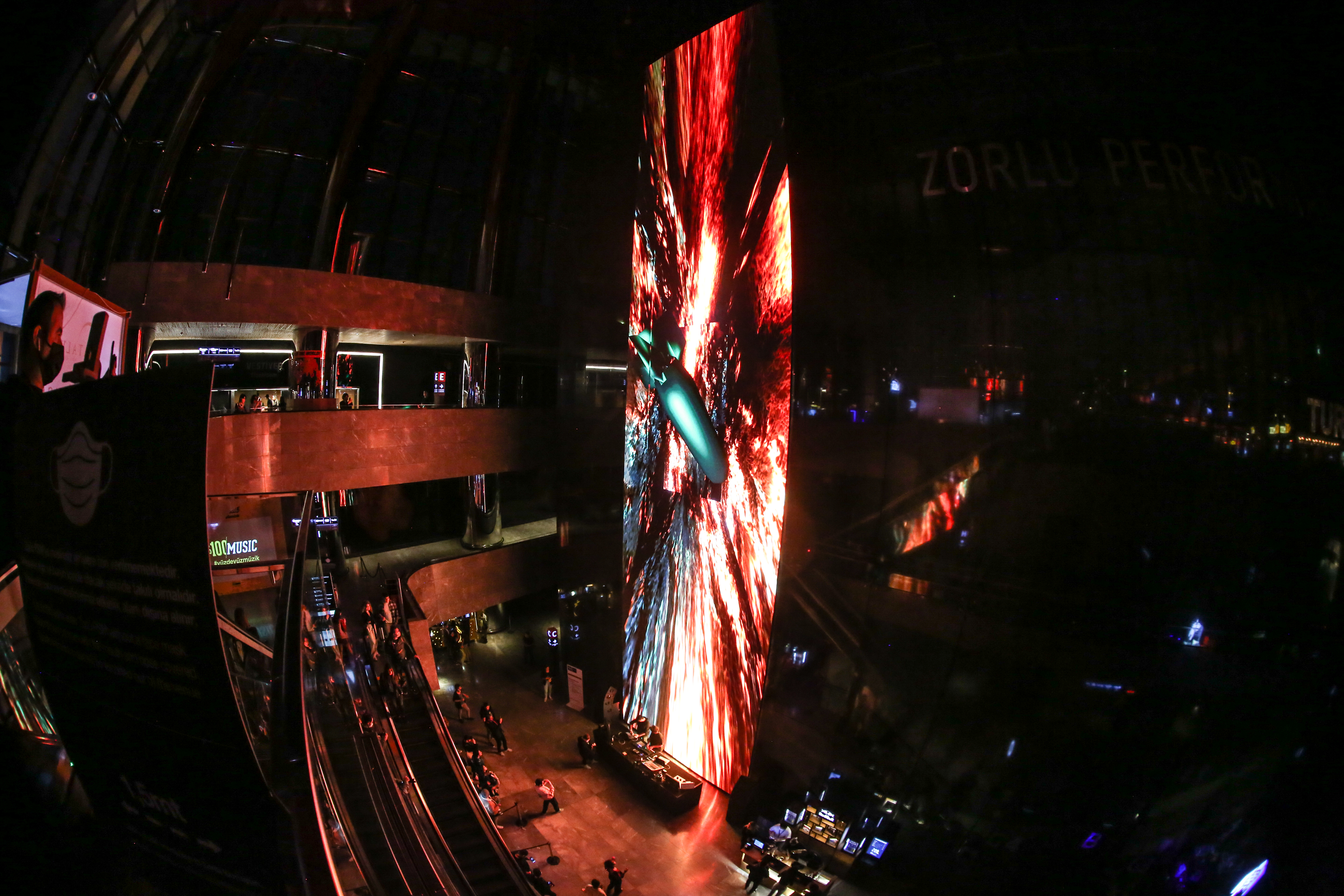 Fisheye view of a large vertical screen with bright red flame-like graphics. Below Huseyin Kuru and Kerem Demirayak navigate the audiovisual tools creating the images.